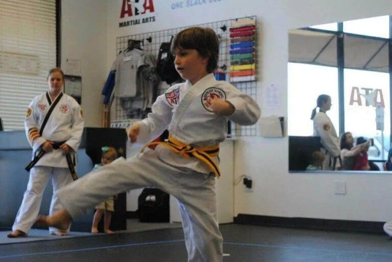 Child executing a focused kick while instructor observes during youth taekwondo training.
