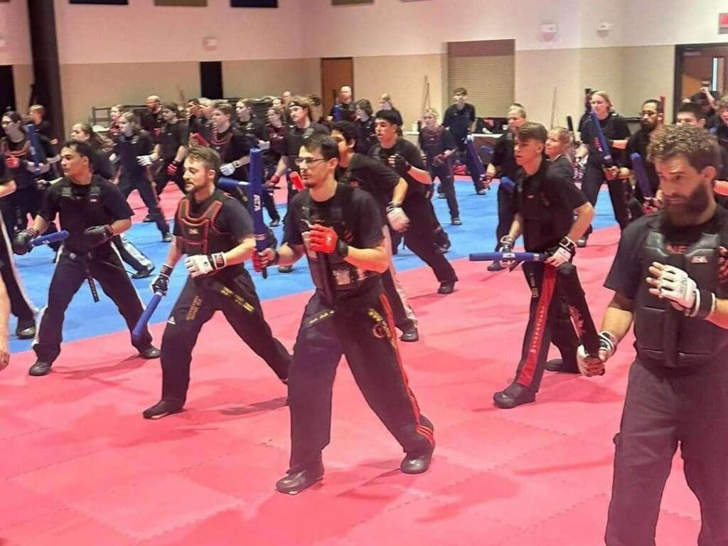 Adult martial arts students practicing weapon defense drills during a large group training session, building skills with an adult martial arts training guide.
