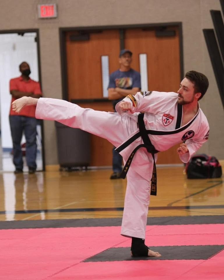 Adult black belt performing a controlled side kick during a martial arts competition, demonstrating technique from an adult martial arts training guide.